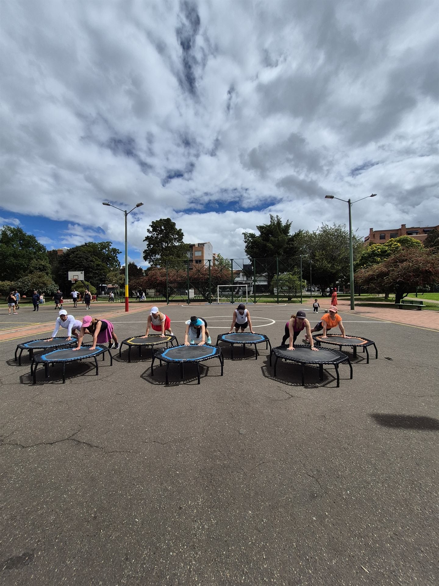 Grupo haciendo plancha sobre trampolines bajo un cielo dramático